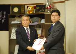 目録授与 左: 釜石市長 野田 武則氏 右: プロダクト企画本部 プロダクト品質管理部長 藤山 尚紀