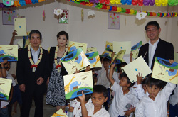 写真: 絵本をプレゼントされ喜ぶ子どもたち (写真左からKDDI財団 伊藤理事長 NPOクロスワイズ横井理事長、KDDI財団梅澤部長)