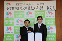 写真: 確認書を取交した (左) 行方市 伊藤市長と (右) KDDI (株) 土橋総務部長