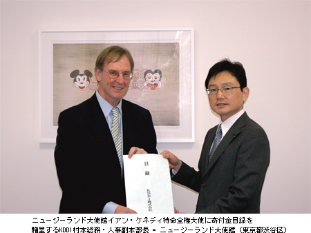 写真: ニュージーランド大使館イアン・ケネディ特命全権大使に寄付金目録を贈呈するKDDI村本総務・人事副本部長 = ニュージーランド大使館 (東京都渋谷区)