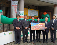 写真: 「高尾山Walk」の総走行距離に応じて鼻が日本一の長さに伸びた「エコ天狗」前での贈呈式の様子