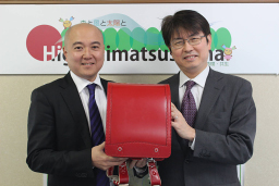 写真: 一般社団法人東松島みらいとし機構 常務理事 赤平久行氏 (左) に贈呈するKDDI 復興支援室室長 阿部博則 (右)