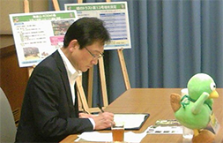 写真: 覚書に署名するKDDI 総務・人事本部 本部長 村本伸一